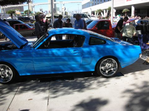 1998 Ford Crown Victoria - bright blue classic fastback coupe with chrome wheels and an open hood sits among spectators at an outdoor show.