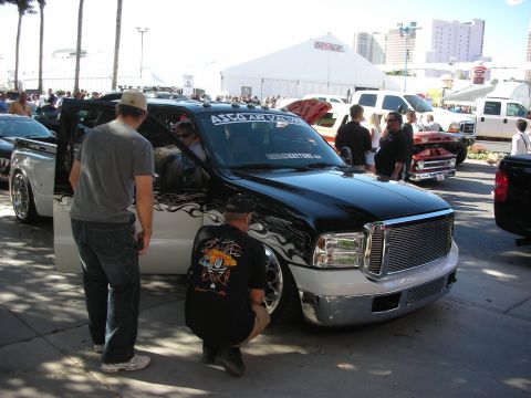 1998 Ford Crown Victoria - lowered black-and-white Ford crew-cab truck with flame graphics draws onlookers at a busy outdoor show.