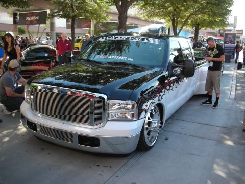 1998 Ford Crown Victoria - slammed black-and-white Ford crew-cab dually with flame graphics and a large chrome grille parked at an outdoor show.