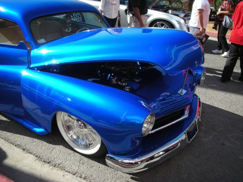 1998 Ford Crown Victoria - bright blue chopped and lowered custom coupe with whitewall tires, chrome bumper and open hood shown at an outdoor car show.