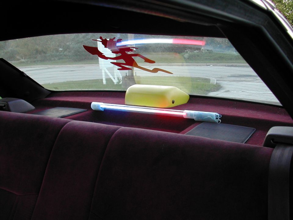 Interior rear deck of a car with a neon tube light and a Devil decal on the back glass