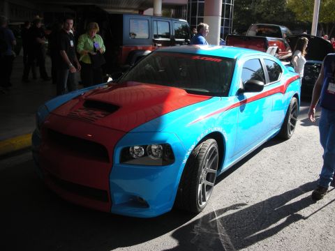 1998 Ford Crown Victoria - blue-and-red two-tone Dodge Charger with a hood scoop and tuning graphics displayed among crowds at an indoor car show.