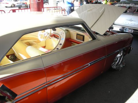 1998 Ford Crown Victoria - custom copper-and-tan lowrider coupe with chrome trim, an open trunk lined in white tufted upholstery, shown indoors at a car show.