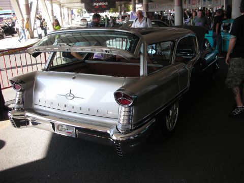 1998 Ford Crown Victoria - Rear three-quarter view of a silver vintage Oldsmobile hardtop with chrome trim and tailfins displayed at an indoor car show.