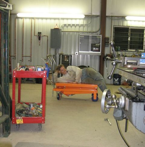 1990 Ford Bronco - A person is lounging on a cart in a workshop, surrounded by equipment and tools.