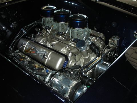 1998 Ford Crown Victoria - polished vintage V8 engine fitted with triple carburetors and a J2 valve cover, mounted in a dark blue engine bay.