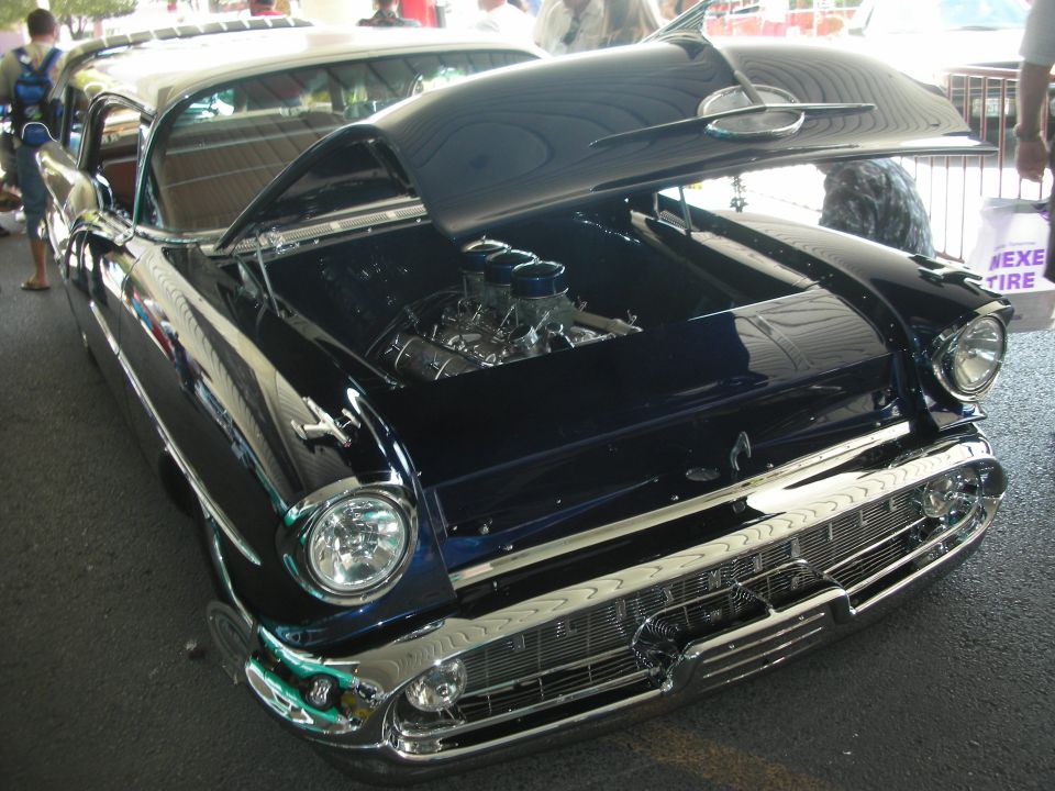 Dark blue 1950s custom hardtop with chrome grille and open hood at outdoor show