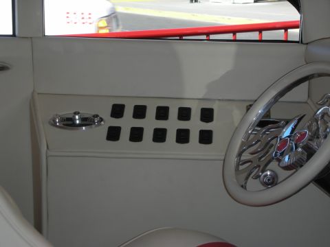 1998 Ford Crown Victoria - Detail of a cream custom car interior showing a black toggle-switch panel and a chrome steering wheel with flame-style spokes.