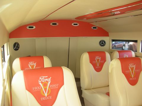 1998 Ford Crown Victoria - Wider view of a custom cabin interior with multiple cream seats bearing Ford V8 Deuce 1932-2007 embroidery beneath a red curved ceiling.