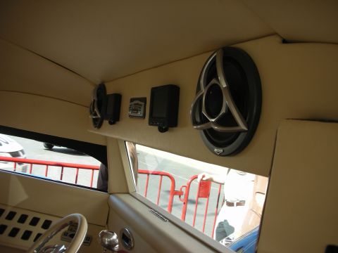 1998 Ford Crown Victoria - Cream-upholstered interior corner of a vehicle showing mounted round speakers and a steering wheel, with a barricaded street seen through t…