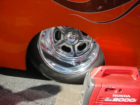 1998 Ford Crown Victoria - Close-up of a polished alloy wheel on an orange car with flame graphics, next to a red Honda EU2000i portable generator.