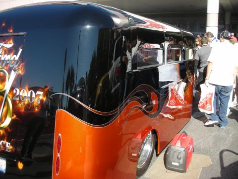 1998 Ford Crown Victoria - Side view of a glossy black and orange custom bus with flame graphics as a crowd gathers, a red generator placed beside the rear wheel.