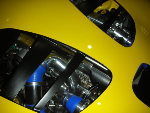 1998 Ford Crown Victoria - Close-up through a yellow car's hood vents showing the engine bay with blue silicone hoses and polished intake piping.