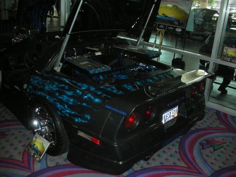 1998 Ford Crown Victoria - Rear of a black Greenwood Corvette with blue flame graphics and a tall wing, plate TSF150, displayed indoors on patterned carpet.