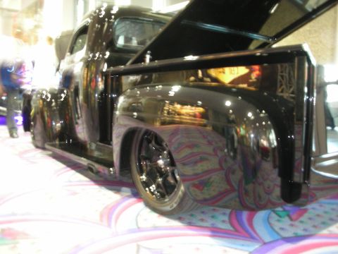 1998 Ford Crown Victoria - Low-angle view of a glossy black lowered custom pickup truck on chrome wheels, displayed indoors on patterned carpet.