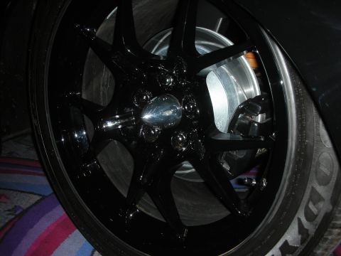1998 Ford Crown Victoria - Close-up of a glossy black multi-spoke alloy wheel with a chrome center cap mounted on a low-profile tire.