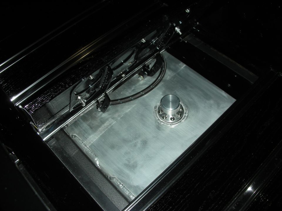 Polished metal fuel cell or tank in a black trunk with braided lines and filler neck