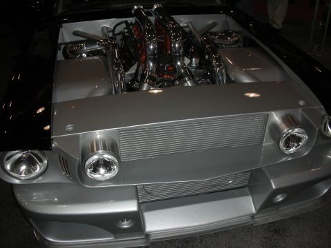 1998 Ford Crown Victoria - Front of a silver muscle car at a show with the hood open, revealing chrome exhaust headers and an engine bay.