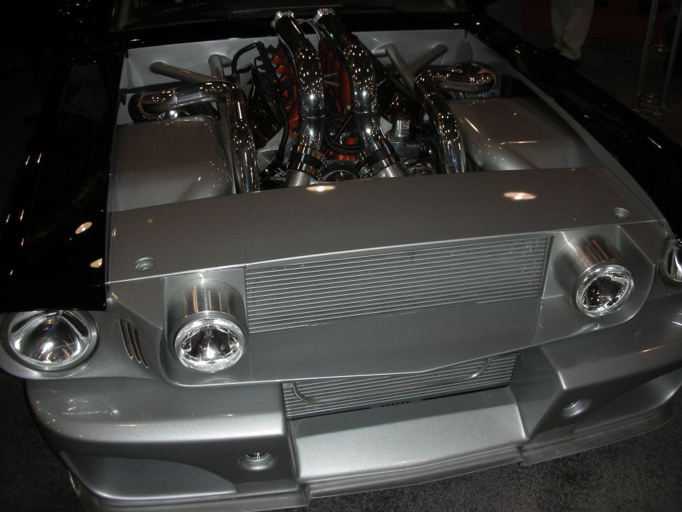 Silver muscle car front end with open hood showing chrome exhaust headers