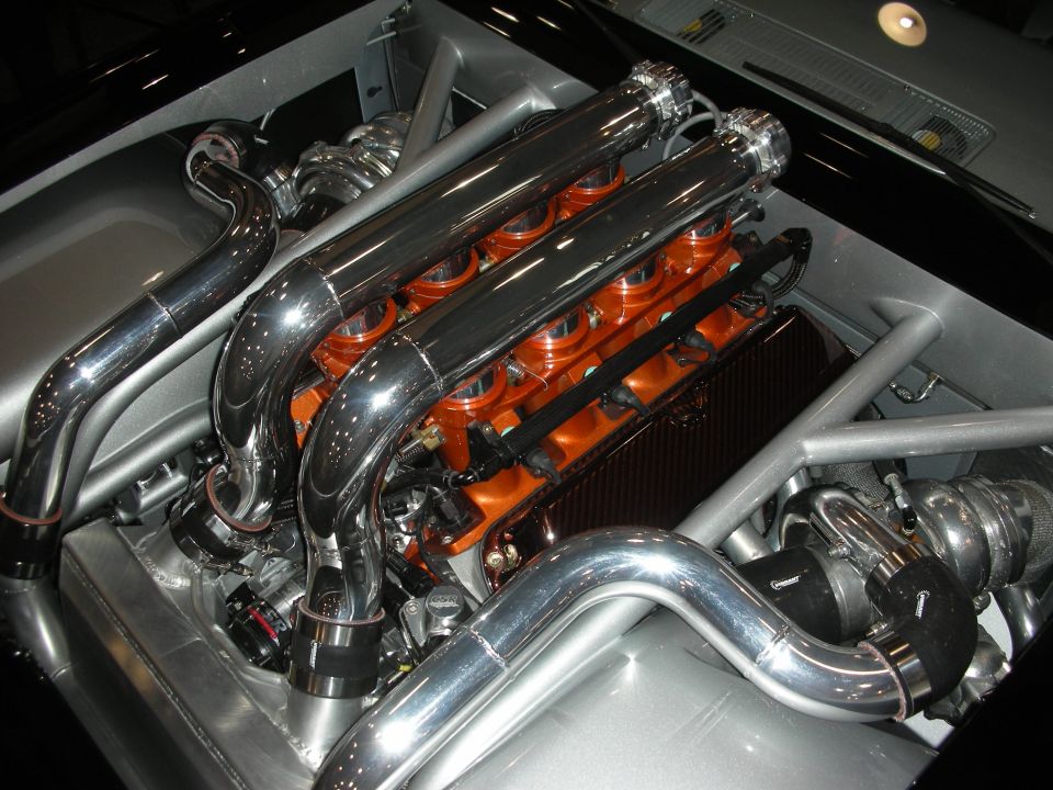 Engine bay with twin polished intake plenums over an orange engine and twin turbos