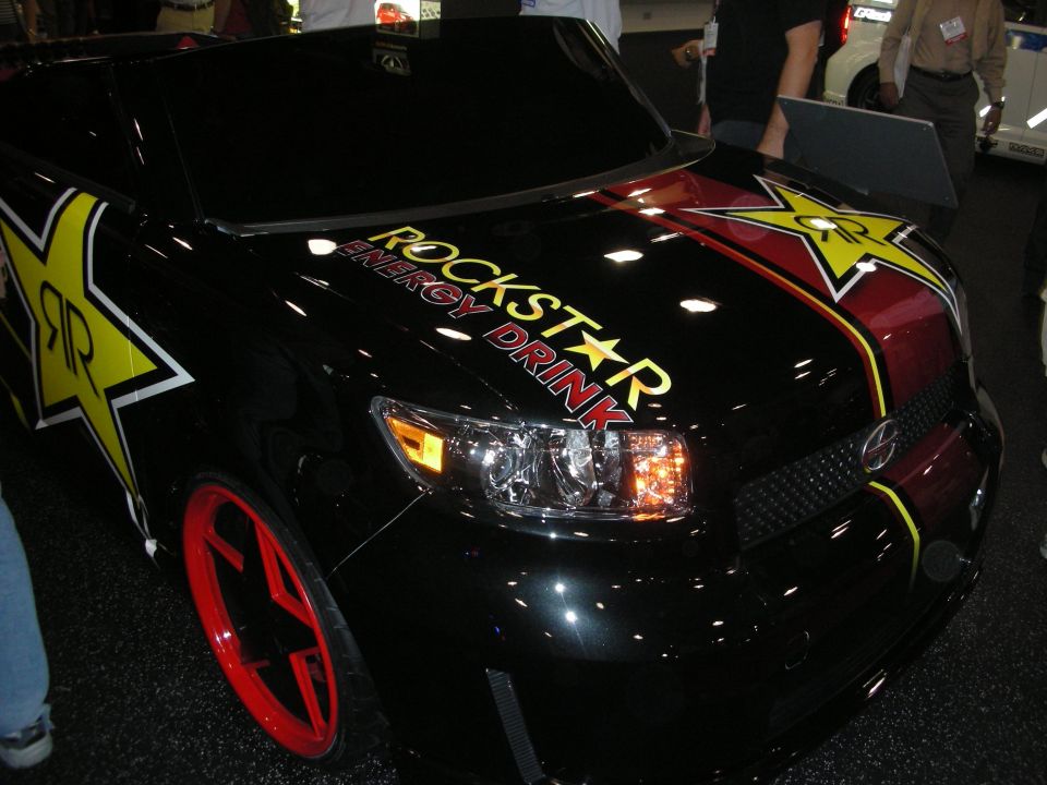 Black Scion with red wheels and Rockstar Energy Drink graphics at a show