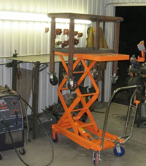 1990 Ford Bronco - An orange scissor lift with a metal frame and wheels is shown in a workshop setting.
