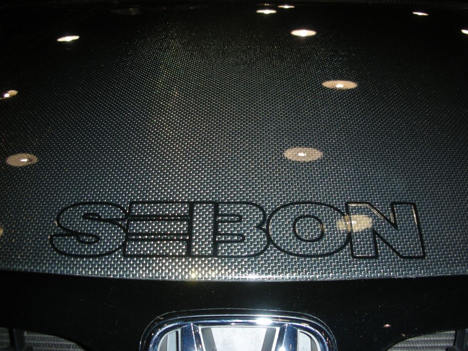 Carbon-fiber Seibon hood over a Honda emblem on a black car