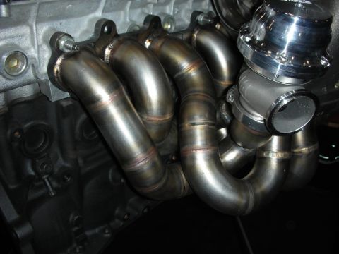 1998 Ford Crown Victoria - welded tubular turbo exhaust manifold with a silver external wastegate bolted to an aluminum engine block.
