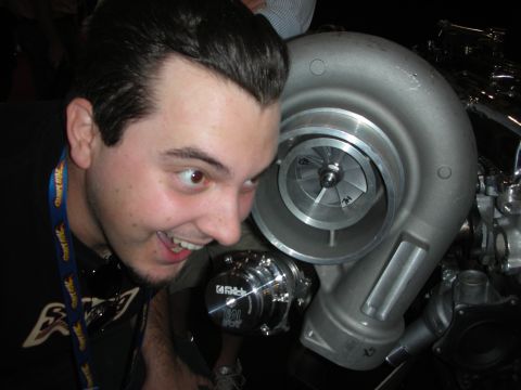 1998 Ford Crown Victoria - grinning young man poses with his face next to a large turbocharger's compressor wheel at an event.