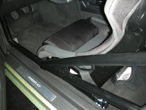 1998 Ford Crown Victoria - car interior footwell showing a gray bucket seat, alloy pedals, roll bar, and an illuminated 'Agent 47' door sill plate.