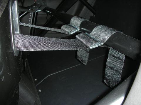 1998 Ford Crown Victoria - Close-up of black racing harness webbing and mounting hardware attached near a vehicle's roll cage and floor.