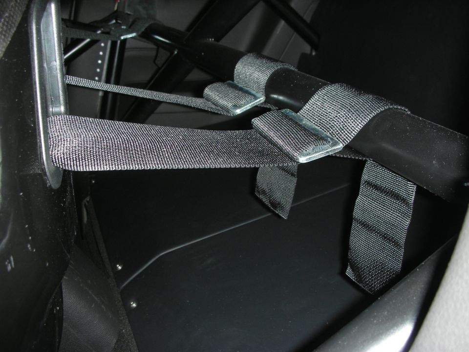 Black racing harness straps and mounting hardware near a roll cage