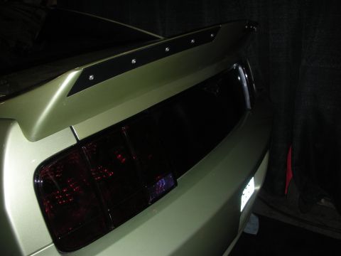 1998 Ford Crown Victoria - Rear quarter of a green late-model Mustang fitted with an adjustable rear wing and smoked tail lights, shot under dim light.