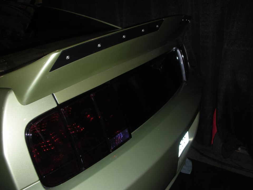 Rear of a green Mustang with adjustable wing and smoked tail lights