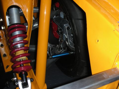 1998 Ford Crown Victoria - Detail of a red coilover shock and a machined brake caliper mounted inside the wheel well of an orange race car.