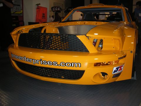 1998 Ford Crown Victoria - Front of an orange Mustang-style race car with a black mesh grille, roll cage, and 'jmeenterprises.com' bumper decals.