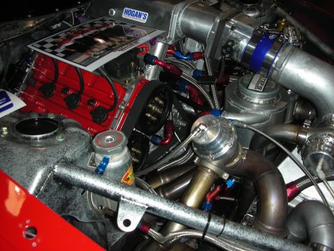 1998 Ford Crown Victoria - Close-up of a built twin-turbo engine showing a red valve cover, blue couplers, braided AN fittings and stainless turbo manifolds.