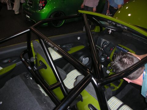 1998 Ford Crown Victoria - interior of a small green car gutted to a black roll cage with houndstooth-trimmed bucket seats, viewed at a show.