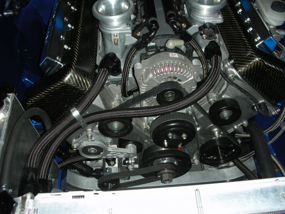 Front of a carbon-covered engine showing alternator, pulleys and braided lines