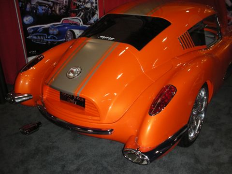 1998 Ford Crown Victoria - orange custom fastback coupe with a silver center racing stripe, chrome bumpers and billet wheels shown at an indoor display.