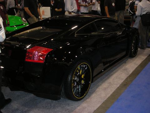 1998 Ford Crown Victoria - black Lamborghini Gallardo coupe shown in rear three-quarter view on black-and-gold wheels with yellow calipers at an expo.