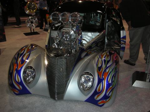 1998 Ford Crown Victoria - chopped silver hot rod with blue flame paint, frenched headlights and an exposed supercharged engine displayed at a show.