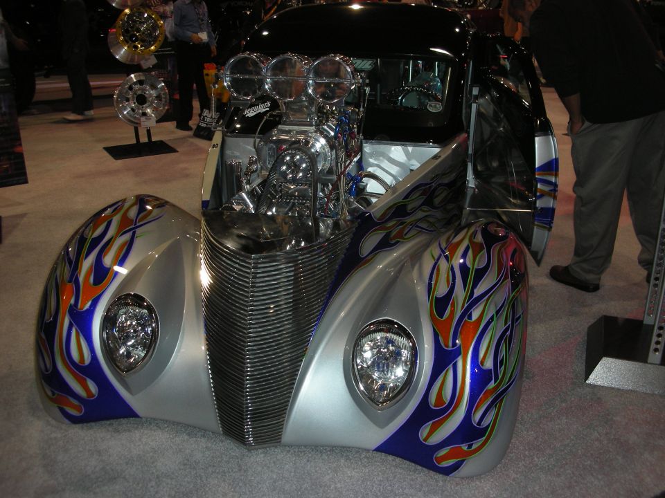 Silver hot rod with blue-and-flame paint and exposed blown engine at indoor show