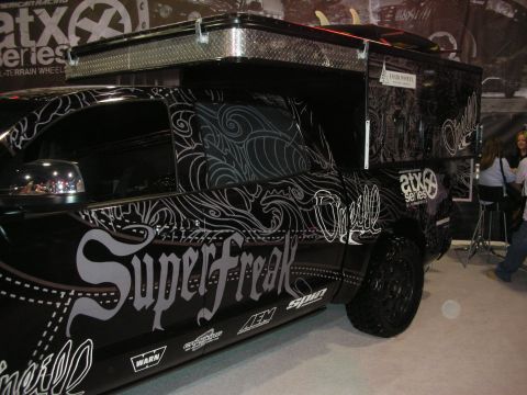 1998 Ford Crown Victoria - black truck wrapped in ornate white filigree and SuperFreak lettering, displayed on ATX wheels at a show booth.