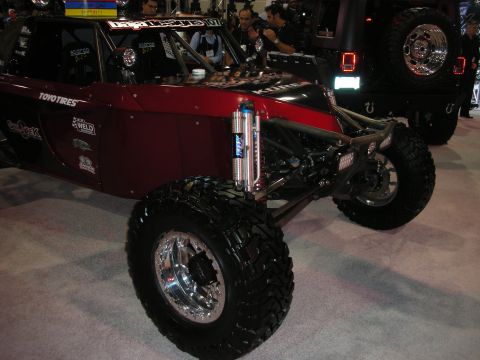 1998 Ford Crown Victoria - dark red tube-chassis off-road buggy on chrome beadlock wheels and Toyo tires, fitted with bypass shocks, displayed indoors.