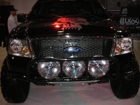 1998 Ford Crown Victoria - black lifted Ford F-150 shown head-on with its blue-oval grille, three round driving lights and a skull graphic on the hood.