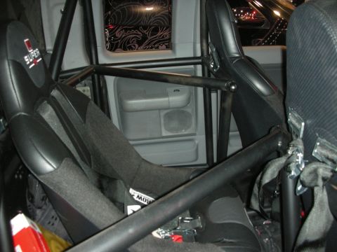 1998 Ford Crown Victoria - caged interior of a customized vehicle showing a black bucket seat and gray door trim framed by black roll-bar tubing.