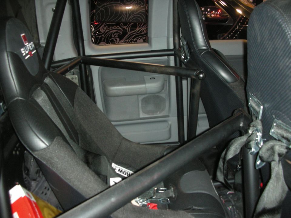 Caged car interior with black bucket seat and gray door panel viewed through roll bars