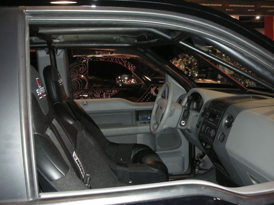 Stripped interior of a custom car with full roll cage, racing bucket seat and gray dash