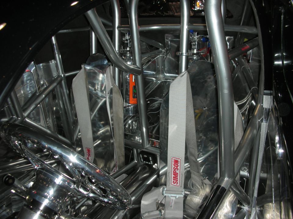 Interior with two aluminum seats, Simpson harnesses and a chrome steering wheel in a roll cage